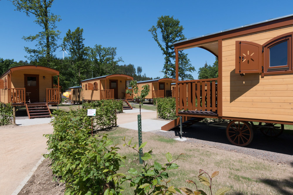 Verschillende houten Naturwagen huisjes op wielen staan op een zonnige dag op een rij, omringd door groen en bomen.