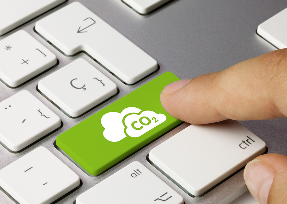 Ein Finger drückt eine grüne Tastaturtaste mit einer Wolke und einem CO2-Symbol, was auf eine Aktion im Zusammenhang mit Kohlendioxid oder ökologischer Nachhaltigkeit hinweist.