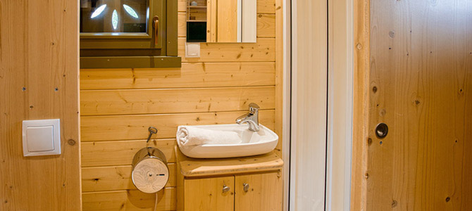 Kleine badkamer in een Naturwagen met houten wanden, een witte wastafel, spiegel erboven, handdoek op de wastafel, toiletpapierhouder en een raam.