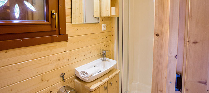 Kleine Naturwagen badkamer met lichthouten muren, een witte wastafel en kast, toiletpapier, een spiegel boven de wastafel en een hoekdouchewand.