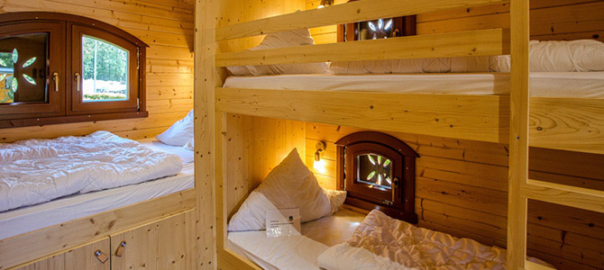 Gezellige Naturwagen: een kleine houten kamer met een eenpersoonsbed en een stapelbed, allemaal netjes opgemaakt met wit beddengoed; twee kleine ramen zorgen voor natuurlijk licht.