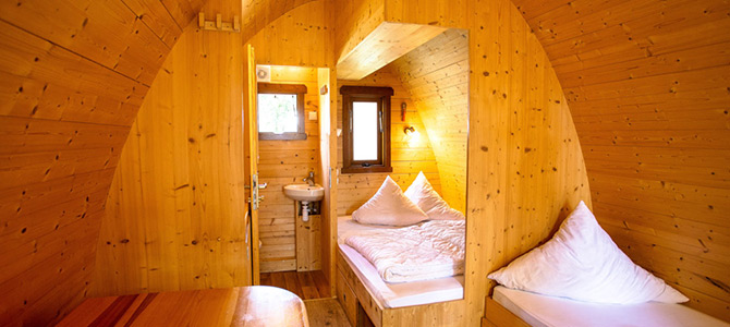 Gezellig interieur in lodge-stijl met een bed met kussens, een opgevouwen deken, een wastafel en een raam dat de ruimte vult met natuurlijk licht.