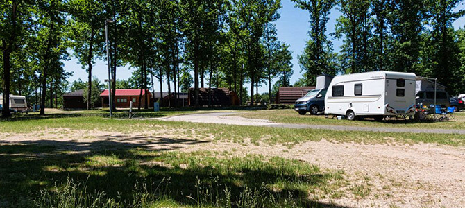 Een camping met verschillende hutten, campers en campers in een Rondell, omringd door bomen op een zonnige dag.